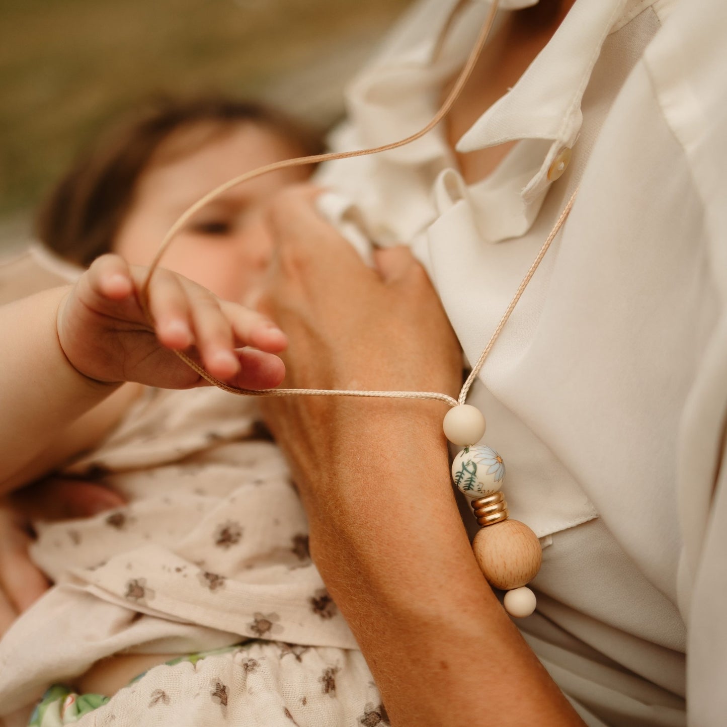 Boho Bloom breastfeeding necklace worn by mum with baby holding it while nursing.
