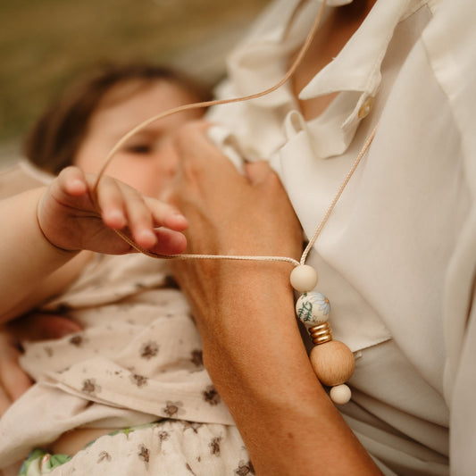Boho Bloom breastfeeding necklace worn by mum with baby holding it while nursing.