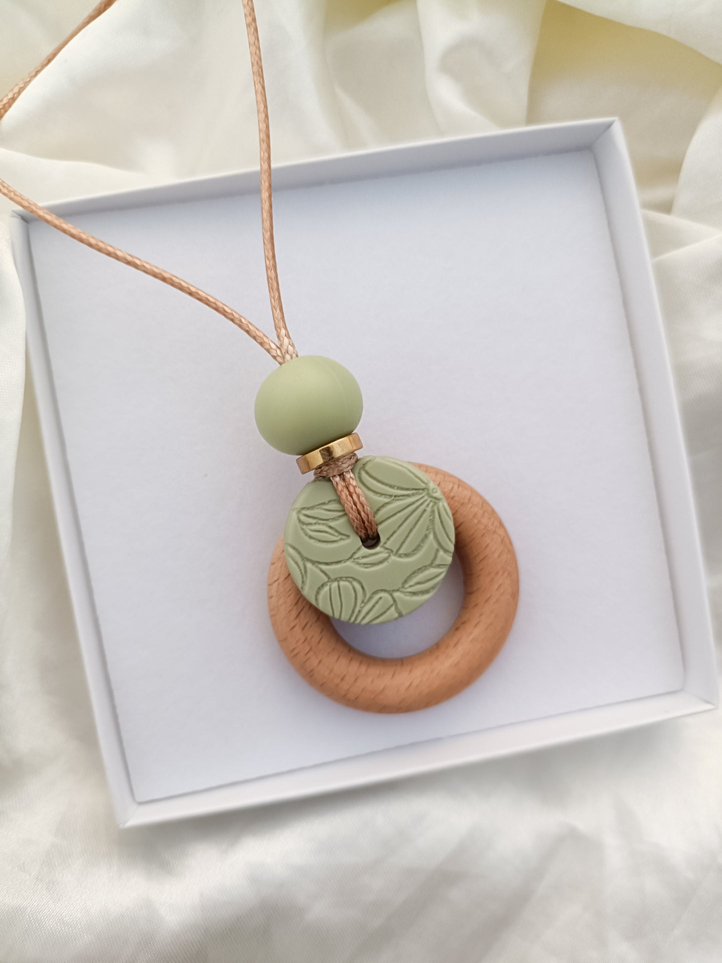 Necklace with green and brown beads in a white box on a white fabric background