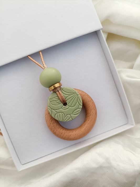 Necklace with green bead and wooden ring in an open white box on a light background